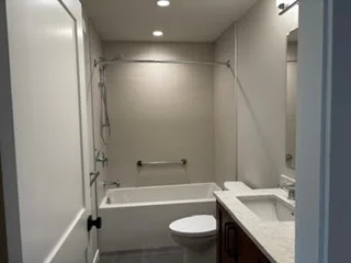 Bathroom with a bathtub, wall-mounted grab bar, shower screen, toilet and vanity