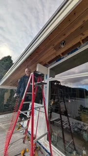 Worker on a red ladder beside exterior windows and a cedar soffit